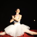 A graceful ballerina executes a perfect split on theater seats, showcasing poise and elegance.